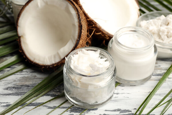 Coconut with jars of coconut oil and cosmetic cream on wooden background