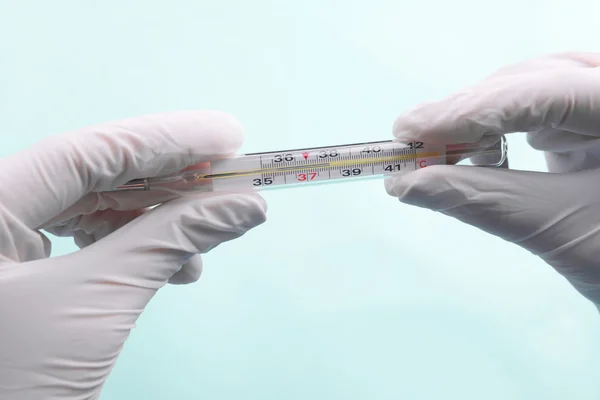 Hands with gloves holding thermometer on blue background — Stock Photo, Image