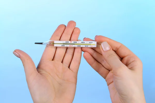 Female hands holding thermometer on blue background — Stock Photo, Image