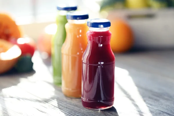 Bottles of juice with fruits and vegetables  on windowsill close up