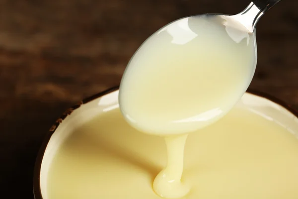 Skål med kondenserad mjölk och sked på bord närbild — Stockfoto