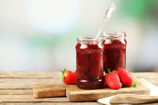 Jars of strawberry jam with berries on table on bright background — Stock Photo, Image