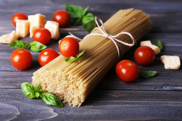 Raw pasta with tomatoes and cheese on wooden background — Stock Photo, Image