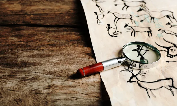 Pinturas rupestres com lupa sobre papel sobre mesa de madeira close-up — Fotografia de Stock