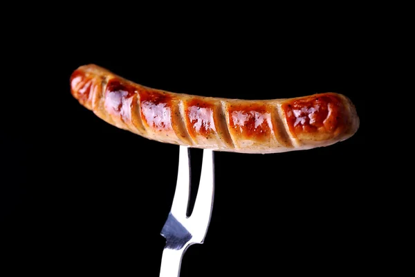 Grilled sausage on fork on black background — Stock Photo, Image