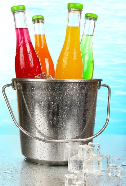 Botellas de bebida sabrosa en cubo de metal con hielo sobre fondo brillante — Foto de Stock