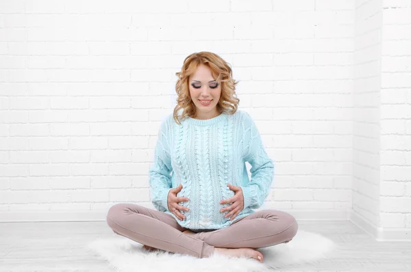 Young pregnant woman sitting on carpet on light background — Stock Photo, Image