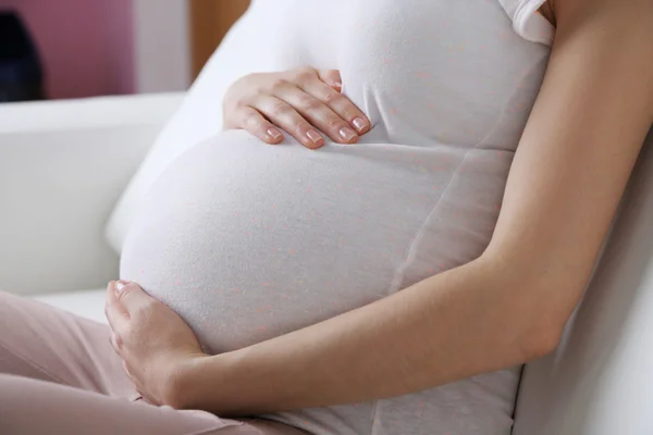 Unga gravid kvinna sitter på soffan på nära håll — Stockfoto