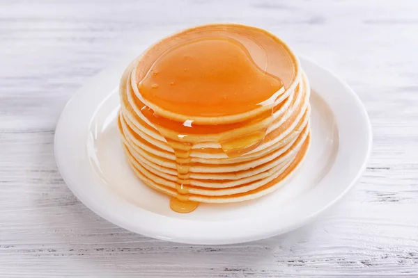 Вкусные блинчики с медом на тарелке на столе крупным планом — стоковое фото