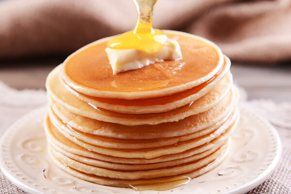 Delicious pancakes with honey on plate on table close-up