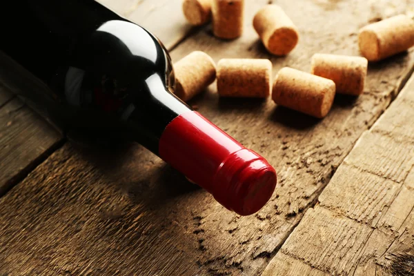 Glass bottle of wine with corks on wooden table background — Stock Photo, Image