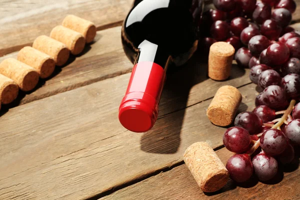 Bouteille de vin en verre avec bouchons et raisins sur fond de table en bois — Photo