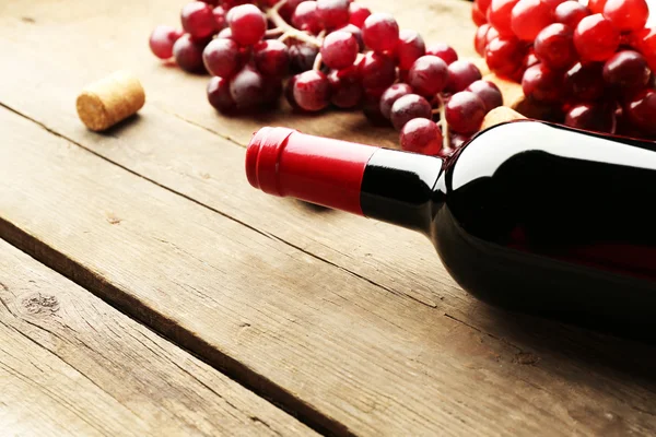 Glasflaska för vin korkar och druvor på träbord bakgrund — Stockfoto