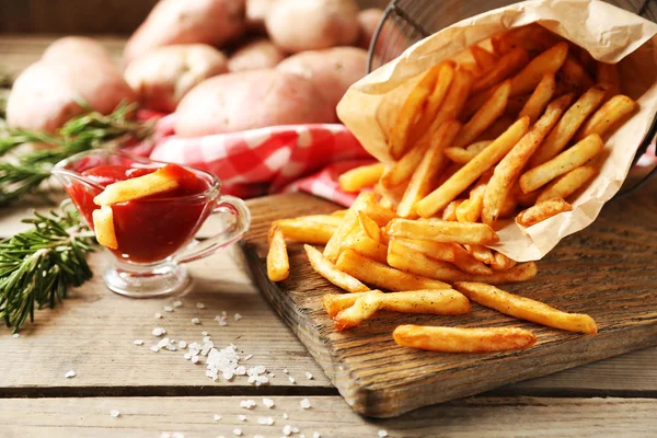 Tasty french fries on cutting board, on wooden table background — Stock Photo, Image