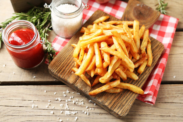 Tasty french fries on cutting board, on wooden table background