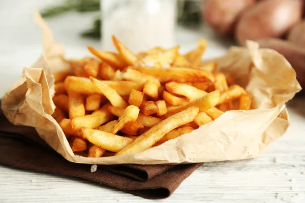 Tasty french fries on paper napkin, on wooden table background — Stock Photo, Image