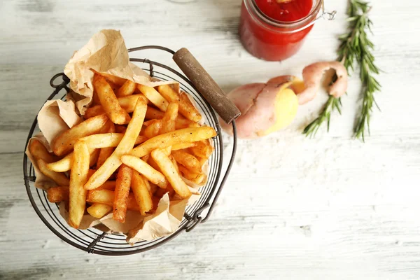 Frites savoureuses dans un panier en métal sur fond de bois de couleur — Photo