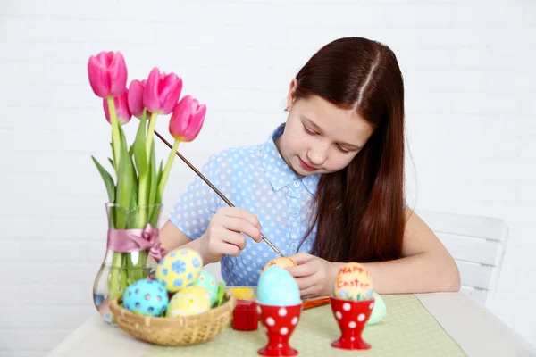 Милая девушка украшает пасхальные яйца, на светлом фоне — стоковое фото