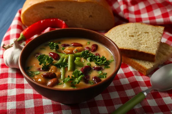 Bean soup in bowl with fresh sliced bread on napkin, on color wooden table background — Stock Photo, Image