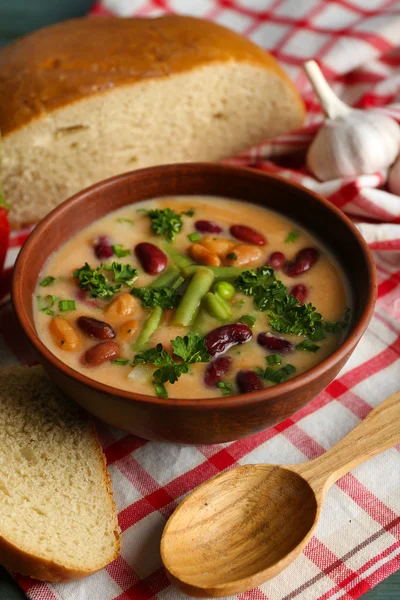 Bean soup in bowl with fresh sliced bread on napkin, on wooden table background — Stock Photo, Image