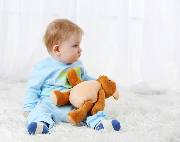 Lindo bebé con oso de peluche en la alfombra, sobre fondo claro —  Fotos de Stock