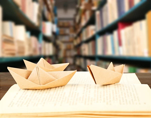 Open book with paper ships on bookshelves background — Stock Photo, Image