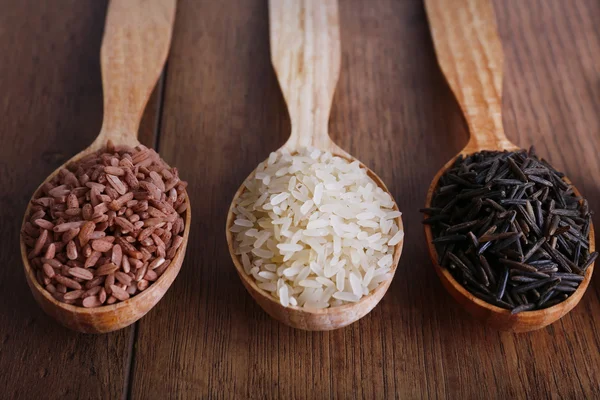 Diferentes tipos de arroz en cucharas sobre fondo de madera — Foto de Stock