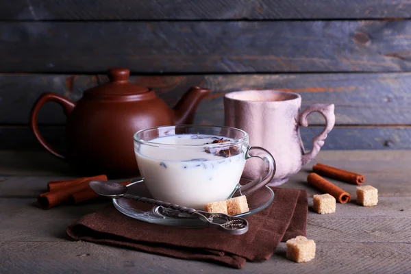 Black tea with milk in cups and teapot with lump sugar on color wooden planks background — Stock Photo, Image