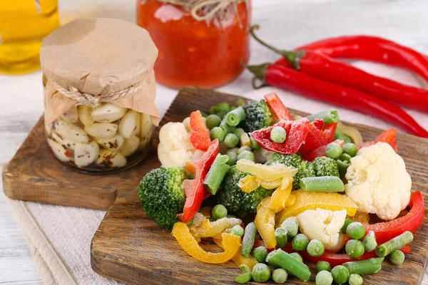 Verduras congeladas sobre tabla de cortar, sobre servilleta, sobre fondo de mesa de madera — Foto de Stock