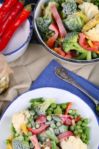 Verduras congeladas en plato sobre servilleta, sobre fondo de mesa de madera —  Fotos de Stock