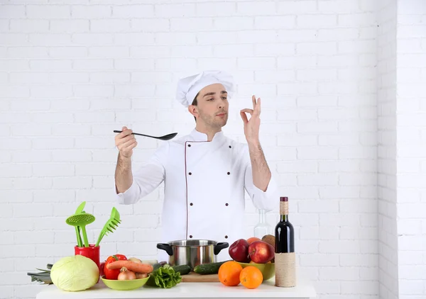 Chef en la mesa con diferentes productos y utensilios en la cocina sobre fondo blanco de la pared —  Fotos de Stock