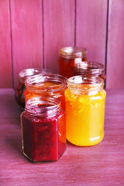 Homemade jars of fruits jam on color wooden background — Stock Photo, Image