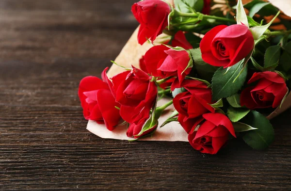 Punaiset ruusut kääritty paperiin puinen pöytä tausta — kuvapankkivalokuva