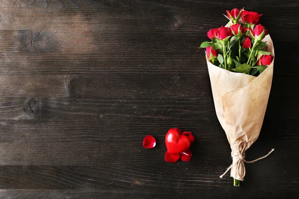 Red roses wrapped in paper with heart on wooden table background — Stock Photo, Image