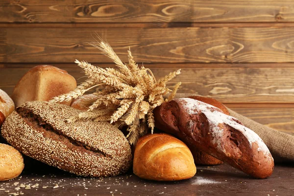 Different bread with ears on wooden background — Stock Photo, Image