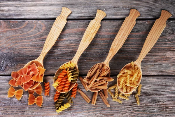 Different types of pasta in spoons on wooden background — Stock Photo, Image