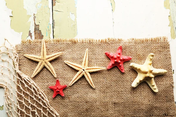 Sea stars on sackcloth on wooden background — Stock Photo, Image