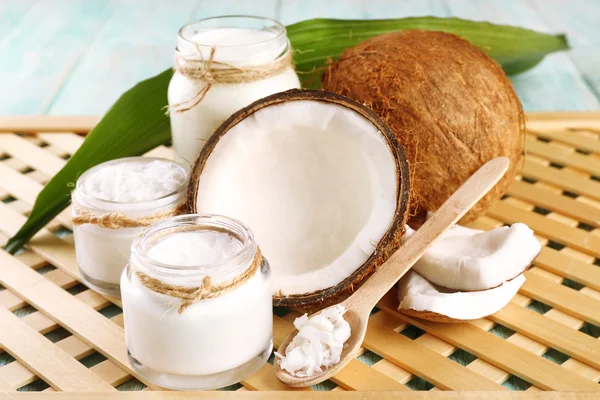 Huile de noix de coco fraîche en verrerie sur fond de table et de grille en bois de couleur — Photo