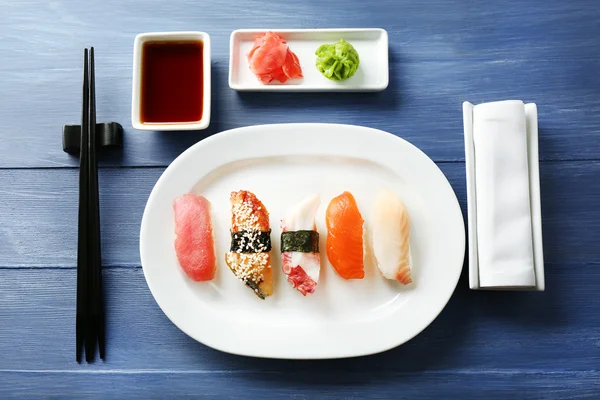 Sushi-Rollen auf Teller, Sojasauce und Essstäbchen auf farbigem Holzhintergrund — Stockfoto