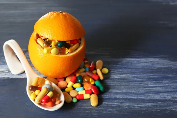 Orange fruit and colorful pills, on wooden background — Stock Photo, Image