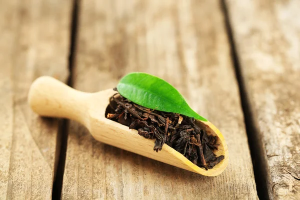 Té negro con hoja en cucharada sobre mesa de madera vieja — Foto de Stock