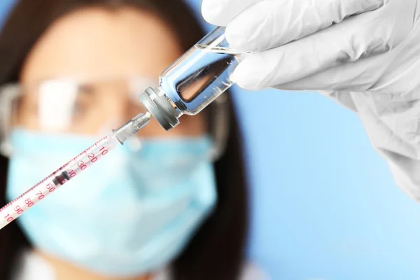 Ampolla y jeringa en manos del médico sobre fondo azul — Foto de Stock