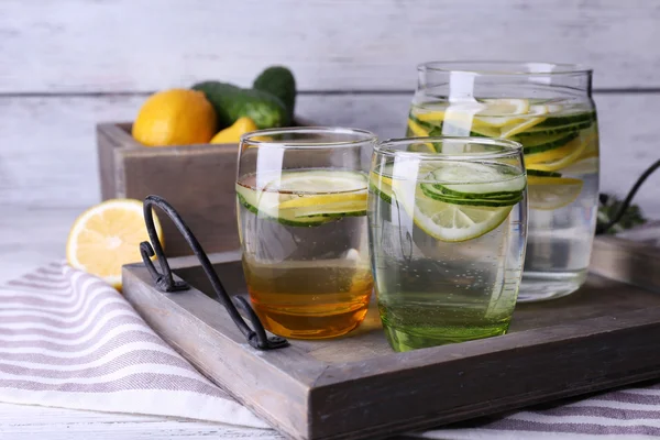 Agua dulce con limón y pepino en cristalería en bandeja de madera, primer plano —  Fotos de Stock