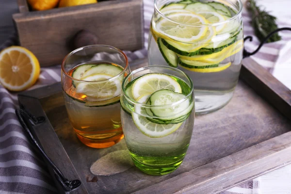 Agua dulce con limón y pepino en cristalería en bandeja de madera, primer plano —  Fotos de Stock