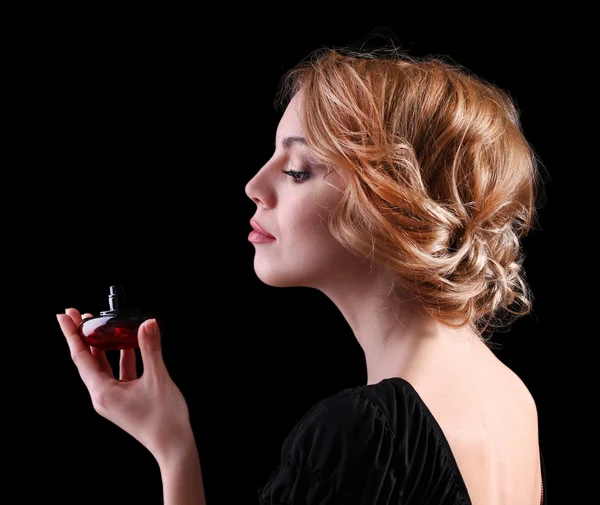 Hermosa joven con botella de perfume sobre fondo negro — Foto de Stock