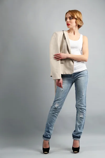 Mooie jonge vrouw in jas en jeans poseren op lichte achtergrond — Stockfoto