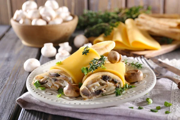 Pancakes with creamy mushrooms in plate on wooden table, closeup