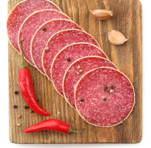 Slices of salami with chili pepper and spices on wooden cutting board isolated on white