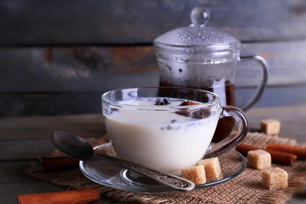 Black tea with milk in glassware and lump sugar on color wooden planks background — Stock Photo, Image