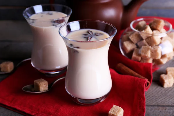 Schwarzer Tee mit Milch in Gläsern und Teekanne mit Klumpen Zucker auf farbigen Holzplanken Hintergrund — Stockfoto